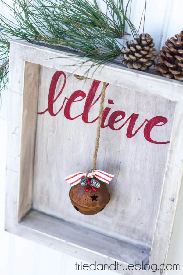 Picture frame with "believe" written in red with pine cones, twigs and a bell